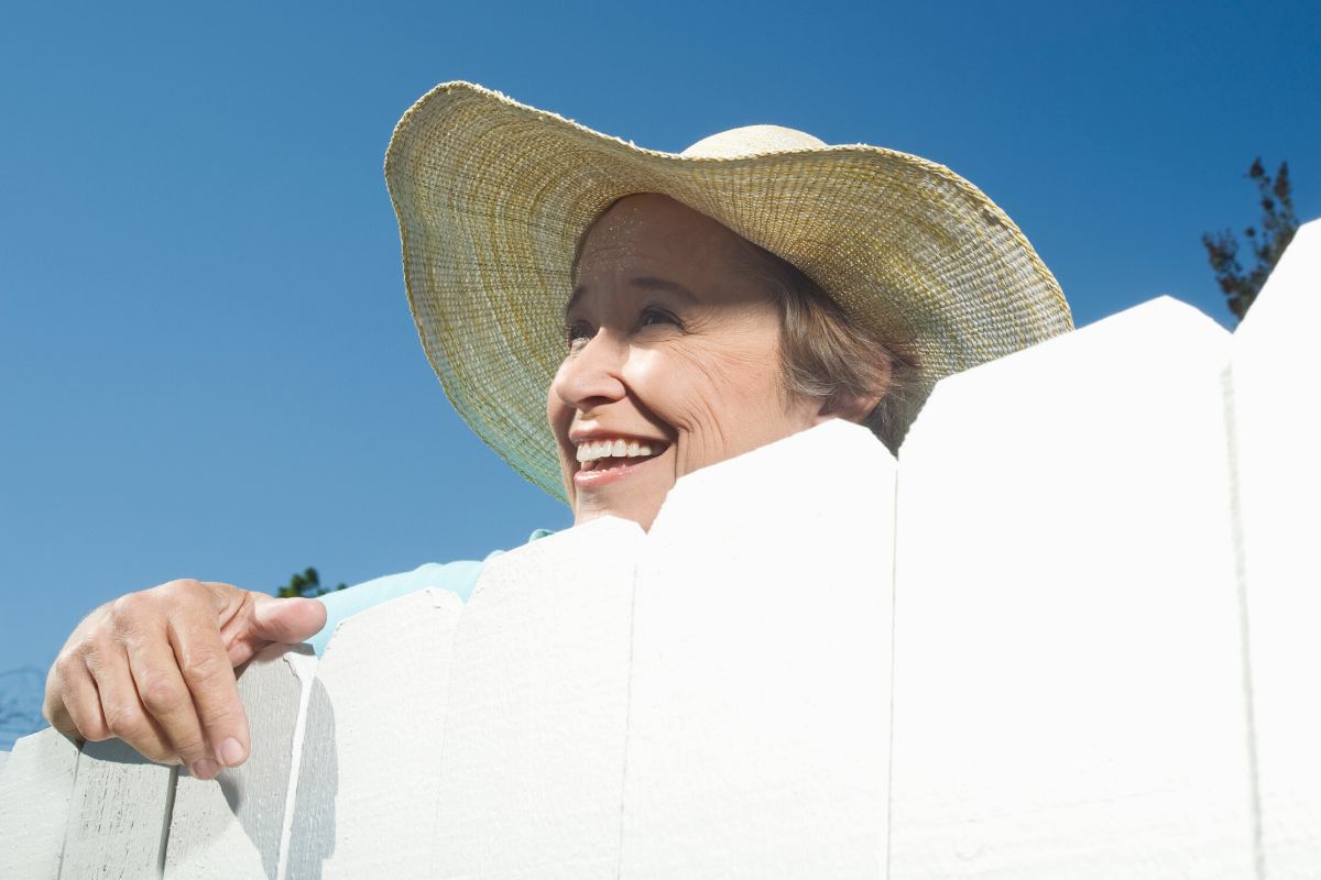 Older woman with a hat on standing by fence